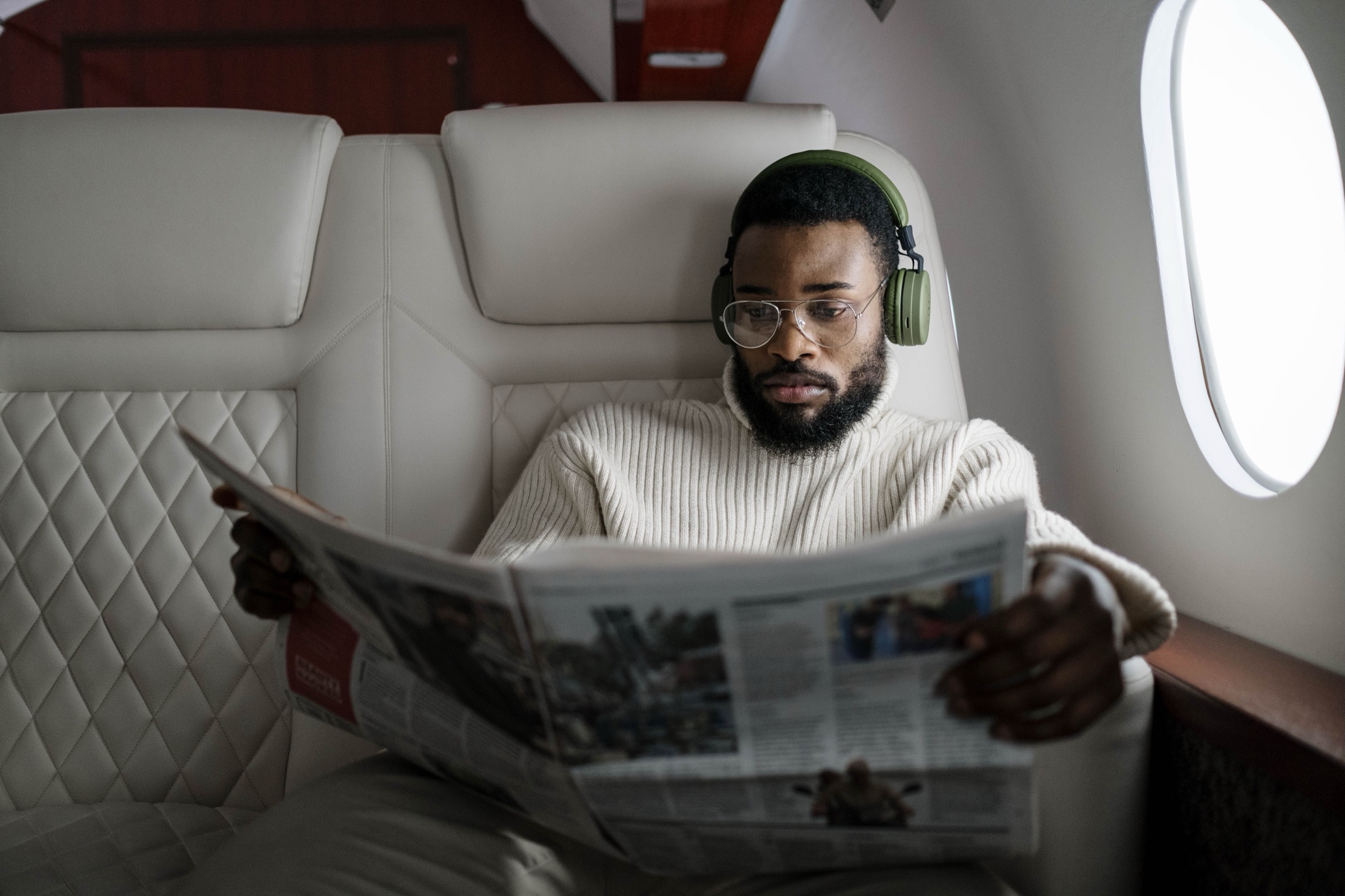Passagier liest Zeitung an Bord eines Privatjets, Blick durch das Kabinenfenster